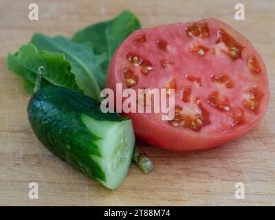 Prodotti freschi, pomodoro Heirloom e cetriolo verde tagliati a metà con polpa, semi e foglie di lattuga, prodotti in casa in un orto Foto Stock