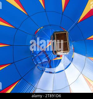 Guardando in alto una mongolfiera blu mentre vola sopra la testa, con una chiara visuale sulla busta della mongolfiera e del cesto del pilota. Foto Stock