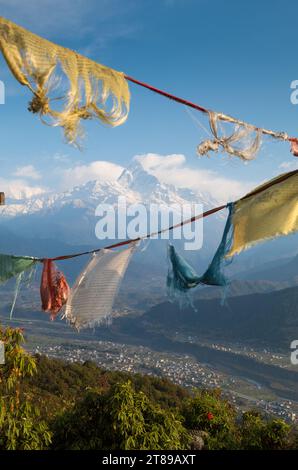 Bandiere di preghiera tibetane pendono su una vista di Machhapuchhare e della valle del fiume Seti, Nepal Foto Stock