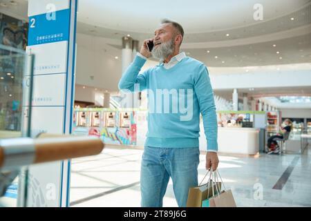 Anziano elegante con telefono che cammina con gli acquisti Foto Stock