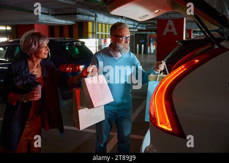 Felice soddisfatta coppia di anziani che caricano gli acquisti nel bagagliaio dell'auto Foto Stock