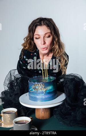 una donna fa saltare le candele su una torta il giorno del suo compleanno Foto Stock