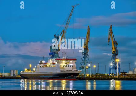 Tre gru gialle e blu al crepuscolo viste nel porto di Belfast, Irlanda del Nord Foto Stock