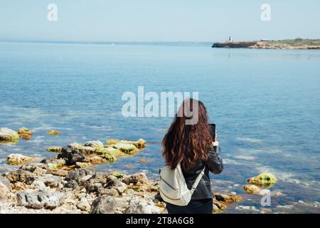 una donna con uno zaino sta in spiaggia con un telefono Foto Stock