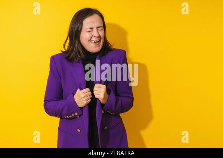 Allegra donna di mezza età che indossa un blazer viola sorridente su sfondo giallo Foto Stock