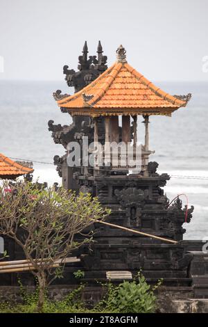 Tempio indù su una spiaggia di sabbia nera direttamente sul mare. Paesaggio serale con onde sul mare sull'isola tropicale di Sanur, Bali, Indonesia Foto Stock