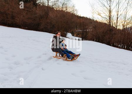 padre e bambino insieme su una slitta di legno che scende sulla collina innevata Foto Stock