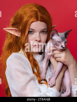 Ritratto di un elfo cosplayer giovane donna in abito bianco, con bellissimi capelli lunghi rossi, occhi di diversi colori che guardano la fotocamera con attenzione Foto Stock