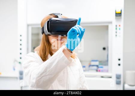 Donna scienziata in occhiali di protezione per la realtà virtuale utilizza la realtà aumentata per effettuare analisi in laboratorio. Foto Stock
