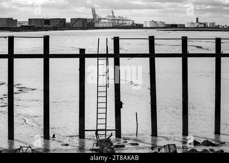 Vista da Canvey Island verso la raffineria di Coryton Oil. Pianure fangose di Holehaven Creek, contenitori per lo stoccaggio di petrolio e DP World Gateway in bianco e nero. Foto Stock