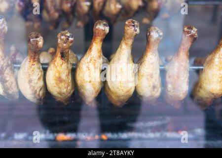 le cosce di pollo vengono fritte nella vetrina di un negozio per la vendita alle persone affamate, affumicate una griglia. Foto di alta qualità Foto Stock