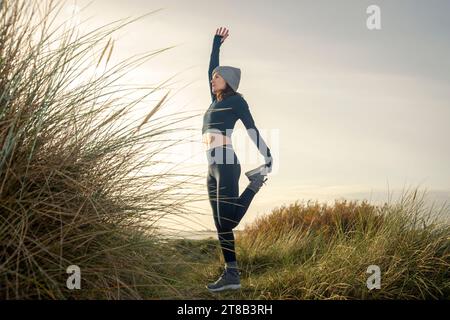 Donna sportiva che allunga le gambe, si allunga la coscia anteriore in piedi e si allunga prima di allenarsi la mattina, Foto Stock