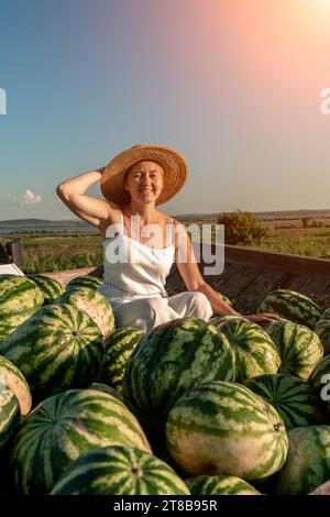 donna anguria. Si siede in un cappello su una montagna di cocomeri. Rimorchio con cocomeri nel mercato. Foto Stock