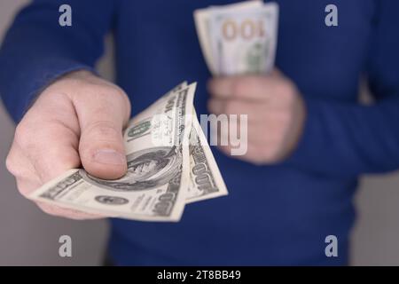 Un uomo con un maglione blu tiene il denaro nelle sue mani, una pila di 100 dollari Foto Stock