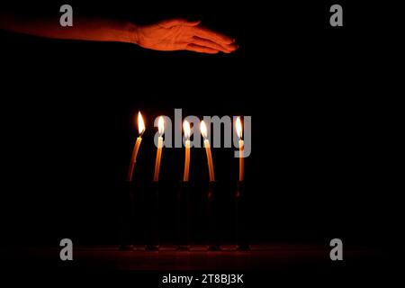 La mano di una donna accanto a involucri in cui le candele bruciano al buio, il dolore e la perdita di persone, la guerra in Ucraina Foto Stock