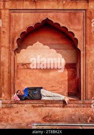 DELHI, INDIA - 20 DICEMBRE 2022: Un uomo non identificato riposa in una nicchia nelle mura di arenaria rossa della moschea Jama Masjid a Delhi, India. Foto Stock