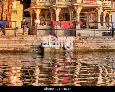 UDAIPUR, INDIA - 27 DICEMBRE 2022: Un uomo e una donna non identificati fanno il bagno sui gradini di un ghat sulla riva del lago Pichola a Udaipur, India. Foto Stock