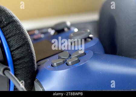 Una foto di un controller console di gioco PlayStation blu scuro e un paio di cuffie su un tavolo bianco. Videogamer. Foto Stock