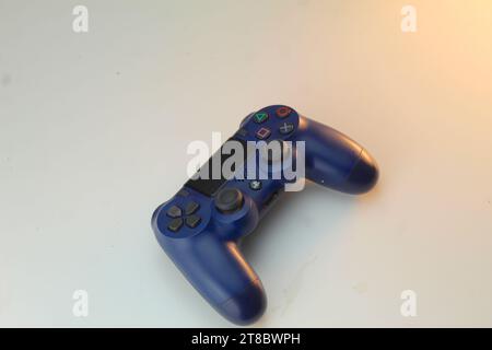 Una foto di un controller console di gioco PlayStation blu scuro e un paio di cuffie su un tavolo bianco. Videogamer. Foto Stock