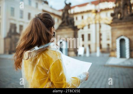 Vista da dietro donna turistica in camicetta gialla e impermeabile a Praga Repubblica Ceca con mappa vicino al Castello di Praga. Foto Stock