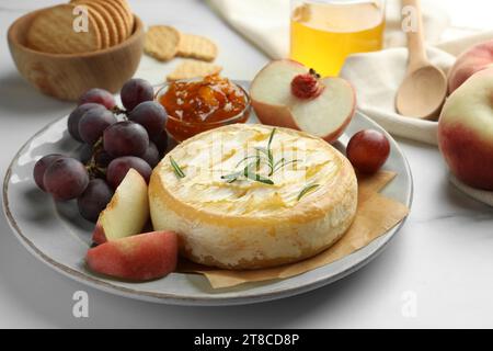 Gustoso formaggio brie al forno con frutta e marmellata su un tavolo di marmo bianco, primo piano Foto Stock