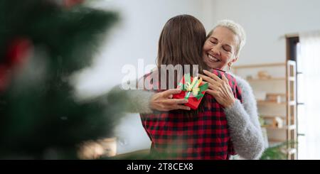 Grata donna caucasica con un regalo di natale che abbraccia la figlia a casa Foto Stock