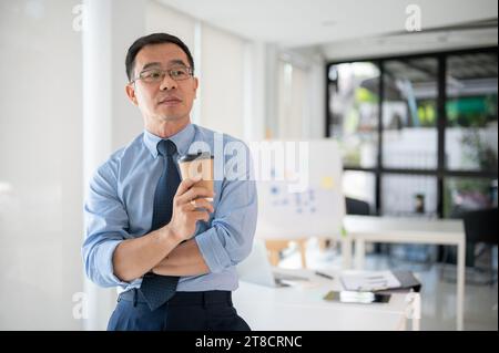 Un uomo d'affari anziano e appassionato che si prende una pausa caffè dopo una lunga giornata di lavoro nel pomeriggio. Foto Stock