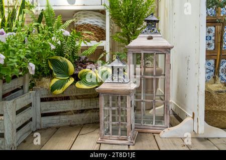 grandi lanterne di vetro con candele all'interno vicino a un letto di fiori con fiori verdi, elemento decorativo del giardino Foto Stock