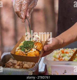 Il venditore sta cucinando la palla giapponese di polipo Takoyaki su una stufa calda. Foto Stock