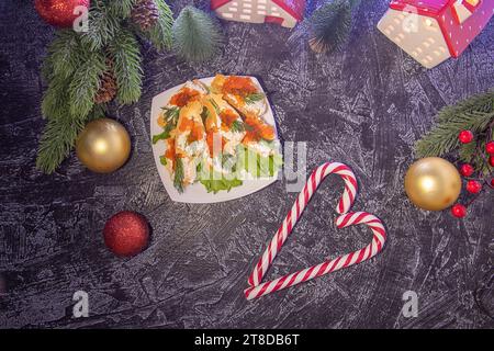 Crostini di antipasti piatti con formaggio cremoso e caviale rosso su uno sfondo nero testurizzato con rami dell'albero di Natale, palline di Natale e bastoncini di caramelle. Serve per una festa di Natale o Capodanno Foto Stock