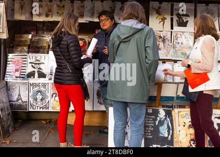 La gente guarda libri e poster mentre cammina davanti a uno stand "bouquinistes" che vende libri antichi e vecchi poster vicino alla riva della Senna a Parigi, il 19 novembre 2023. I librai parigini, la più grande libreria all'aperto del mondo, che operano sulle rive della Senna da 450 anni, si rifiutano di essere spostati dalle autorità per garantire la sicurezza per la cerimonia di apertura dei Giochi Olimpici di Parigi 2024. Installati lungo più di tre chilometri della Senna e dichiarati patrimonio dell'umanità dell'UNESCO, i 240 bouquinistes utilizzano 900 scatole verdi per ospitare circa 300.000 vecchi libri Foto Stock