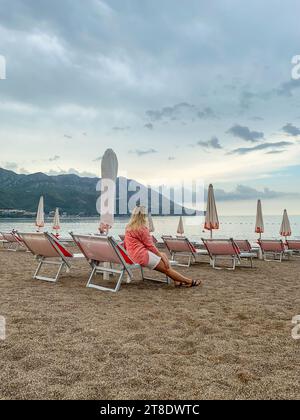 Donna seduta su un lettino su una spiaggia vuota la mattina presto Foto Stock