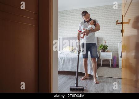 Padre che tiene un bambino sbadigliante mentre pulisce la casa Foto Stock