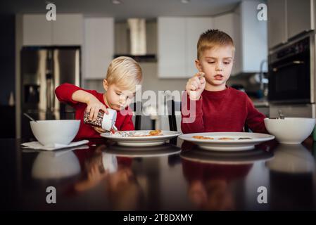 Due fratelli che indossano camicie rosse si siedono al tavolo per decorare biscotti Foto Stock