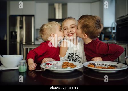 Primo piano di due ragazzi che baciano la sorella sulla guancia mentre si siedono Foto Stock