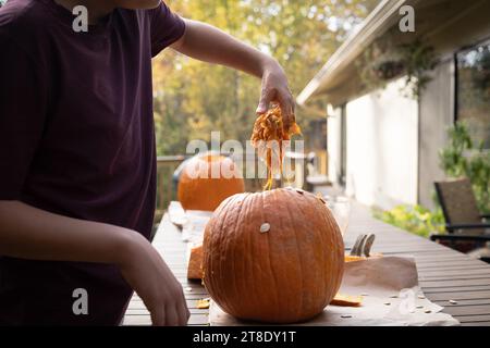 Ragazzo che rimuove la polpa e i semi dalla zucca prima di intagliare la faccia spettrale. Foto Stock