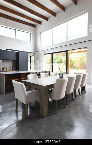 Grande cucina vuota con tavolo in legno, sedie bianche e grandi finestre Foto Stock