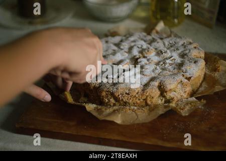 La mano di una donna taglia una torta di mele Charlotte pronta in parti uguali con un coltello in cucina su una tavola di legno Foto Stock