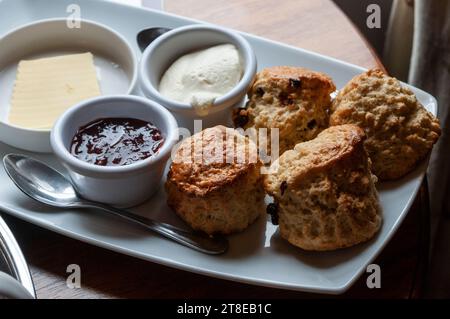 Quattro focaccine irlandesi al burro, appena sfornate, servite su un piatto con burro, marmellata e panna coagulata Foto Stock