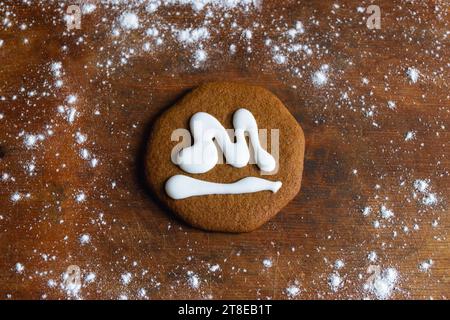 Un biscotto dolce al pan di zenzero ricoperto di glassa bianca a forma di lettera M si trova su una vecchia tavola circondata da farina Foto Stock