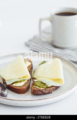 Tostate con burro, pesto e formaggio su un piatto bianco. Concetto di colazione. Foto Stock