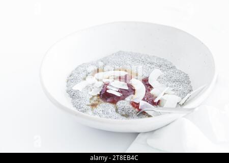 Budino di Chia con marmellata e patatine di cocco in un piatto bianco, primo piano. Colazione vegana. Foto Stock