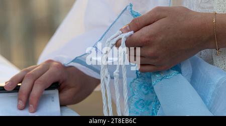 Primo piano di un uomo ebreo che prega mentre tiene le corde o tzit-tzit sul suo tallit in mano e recita lo shemà yisrael. Foto Stock