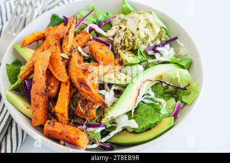 Spicchi di patate dolci al forno con salsa di avocado e hummus. Insalata pranzo vegana sana. Foto Stock