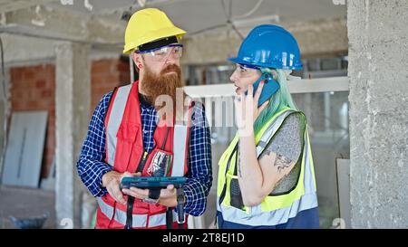 Uomini e donne costruttori che parlano su smartphone utilizzando il touchpad in cantiere Foto Stock