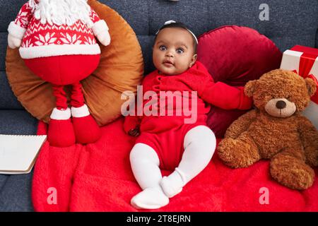 Bambino afro-americano sorridente seduto sul divano con la bambola di babbo natale a casa Foto Stock