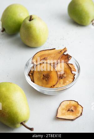 Fette di peri seccate e ambrate in un recipiente di vetro con pere verdi su un tavolo leggero. Foto Stock