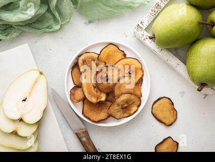 Fette di pera secche in piastra con pere mature verdi e coltello su sfondo chiaro. Foto Stock