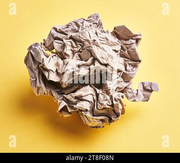 Una pallina di carta marrone sgualcita su sfondo giallo isolato Foto Stock