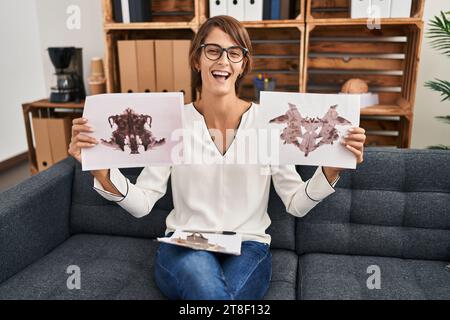 Bruna donna che lavora con il test di rorschach alla clinica di psicologia sorridendo e ridendo a voce alta perché divertente scherzo folle. Foto Stock